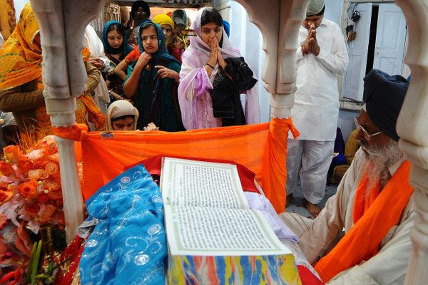Pakistani and Indian Sikh devotees gather around a priest reading from the Sikh holy book to celebrate the birthday of Sri Guru Nanak Dev, in Nankana Sahib. 